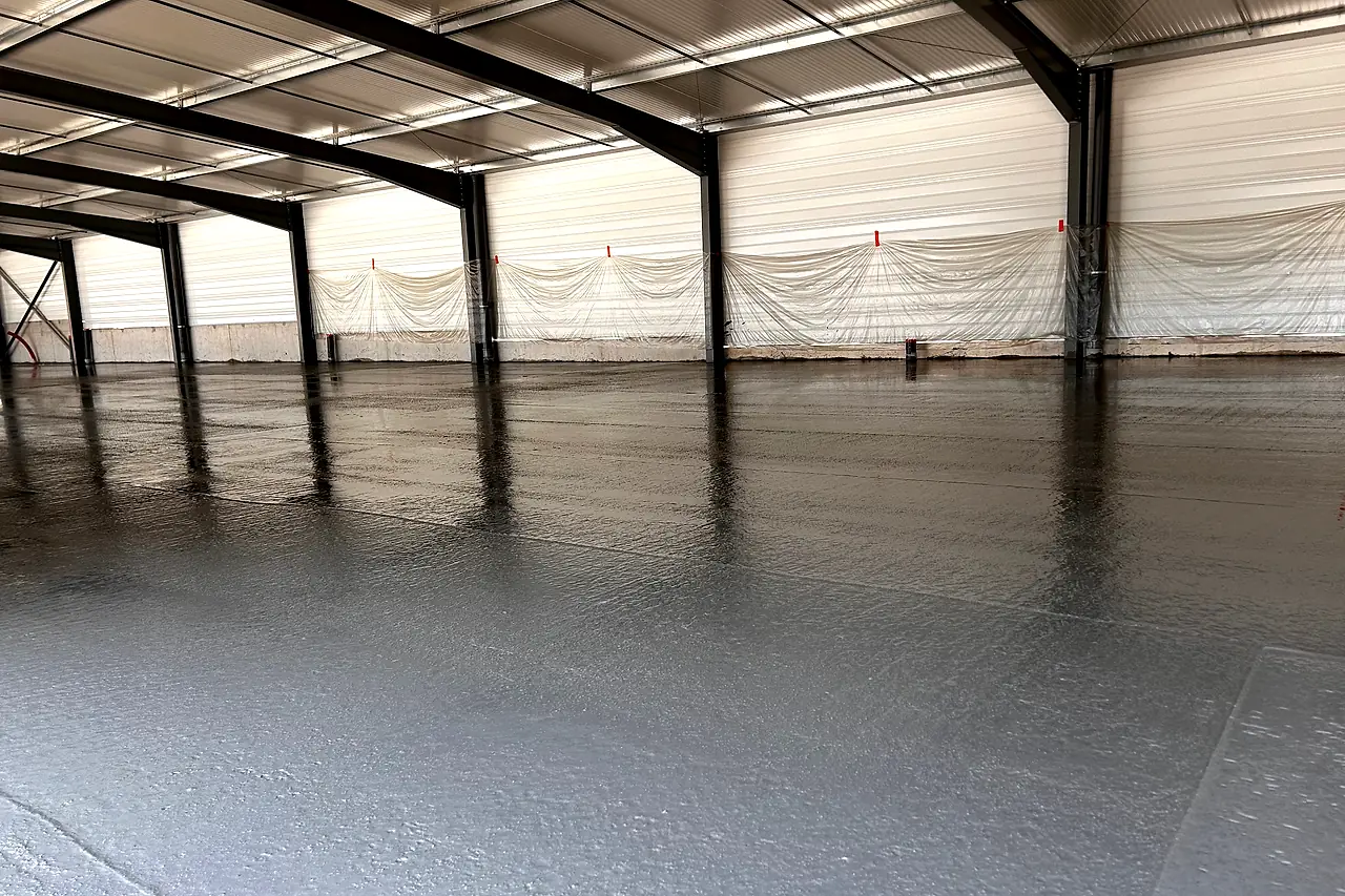 Dalle béton fraîchement lissée dans le bâtiment de Cevenn’Menuiserie à Saint-Ambroix, sous la charpente métallique