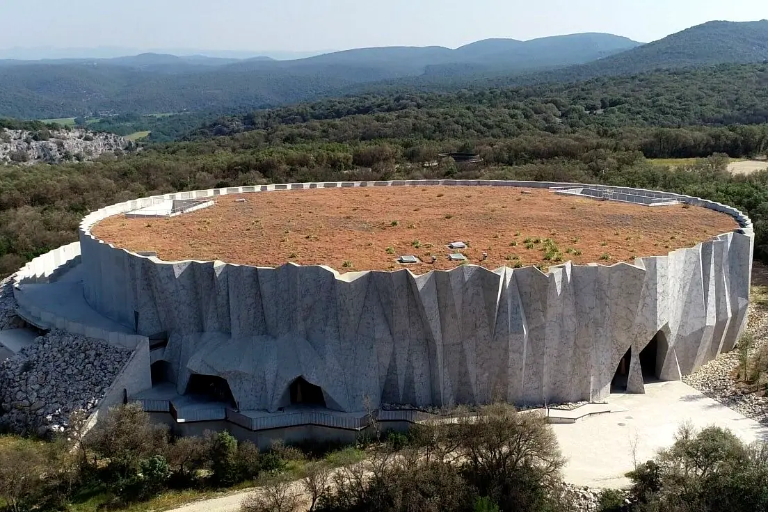 La Grotte Chauvet 2 vue du ciel, façade en béton aux reliefs de roche et toiture végétalisée, au milieu de la garrigue
